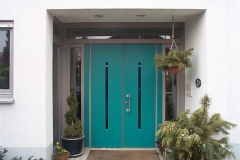 Doppelflüglige Haustür, Rahmen grau lasiert, Türblätter Türkis lackiert. Glasstreifen Kobaltblau
